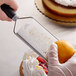 A person using a Mercer Culinary stainless steel zester to grate a lemon over a cake.
