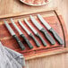 A group of Choice jumbo stainless steel steak knives with black handles on a cutting board.