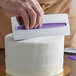 A hand using Wilton stainless steel icing comb to decorate a white cake.