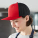 A woman in a red and black apron smiling while wearing a red and black Mercer Culinary trucker hat.