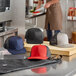 A man wearing a red and black Mercer Culinary trucker cap with a mesh back on a counter in a professional kitchen.