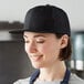 A woman wearing a black Mercer Culinary trucker cap in a professional kitchen.