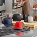 A man in a brown apron wearing a black Mercer Culinary trucker cap with a mesh back on a table.