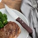 A steak and broccoli on a plate with a Choice jumbo steak knife.