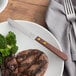A plate with a Choice stainless steel steak knife and steak and broccoli.