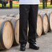 A person wearing black Uncommon Cargo Chef pants standing in front of barrels.