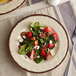 A Carlisle Mingle Sweet Cream melamine salad plate with a salad of strawberries and pecans.