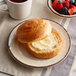 A Carlisle sweet cream melamine bread plate with a roll and butter on it.