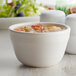 A close-up of a Tuxton white China bouillon cup filled with soup on a table.