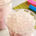 A close-up of a pink drink with ice cubes and a straw.