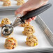 A hand using a Hamilton Beach black thumb press scoop with yellow cookie dough over cookies.