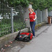 A woman using a Bissell Commercial outdoor power sweeper to clean the street.