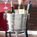 A hand holding a bottle of wine in a stainless steel wine bucket filled with ice.