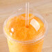 A Fabri-Kal Greenware plastic cup lid with a straw in it over orange liquid.