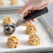 A hand using a Hamilton Beach black thumb press disher to scoop cookie dough.