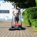 A man using a Bissell Commercial Triple Brush Manual Power Sweeper to clean a sidewalk.