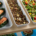 A white Cambro market pan filled with a variety of vegetables on a buffet counter.
