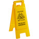 A yellow Carlisle wet floor sign with black text in English and Spanish.