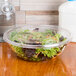 A Sabert FreshPack clear plastic lid on a shallow round bowl filled with salad.