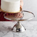 A woman holding a cake on a Vollrath stainless steel cake stand.