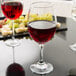 A close up of a Libbey tall wine glass filled with red wine on a table with grapes.