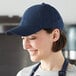A woman wearing a Mercer Culinary navy blue 6-panel baseball cap in a professional kitchen.