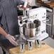 A person in a grey coat using the Avantco #5 Hub Meat Grinder attachment on a mixer to grind meat.