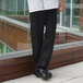 A person wearing black Uncommon Chef 4020 executive chef pants and a white coat on a professional kitchen counter.