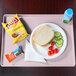 A Cambro blush dietary tray holding a plate of food with a sandwich and vegetables and a bottle of water.