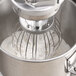 An Avantco MIX8 series mixer with a wire whisk attachment mixing white liquid.