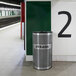 A stainless steel Ex-Cell Kaiser round perforated trash receptacle in a subway station.