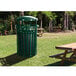 An Ex-Cell Kaiser Hunter Green outdoor trash receptacle on a grassy area beside a picnic table.