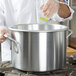 A person in a white coat using a Vollrath Wear-Ever aluminum sauce pot.