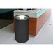 An Ex-Cell Kaiser black steel round waste receptacle on a white counter.