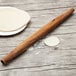 A Fox Run acacia wood French rolling pin on a wood surface with a plate of flour.