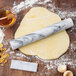 A Fox Run white marble rolling pin on dough with ingredients on a wooden table.