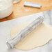 A Fox Run white marble rolling pin on a roll of dough on a marble surface.