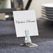 A stainless steel clamp-style menu/card holder on a table with a sign in it.