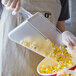 A person using a Carlisle clear polycarbonate utility scoop to pour popcorn into a bowl.