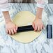 A person using a Fox Run black marble rolling pin on a white surface to roll out dough.