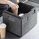 A person putting a coffee cup into a black Cambro food pan carrier with cup holders.