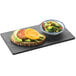 A black rectangular slate serving stone with a sandwich and salad on a table.