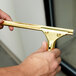 A person holding a Unger GoldenClip window squeegee with a brass handle.