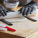 A person wearing black gloves uses a black rectangular fondant leveler to roll out dough on a table.