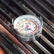 A round metal CDN grill thermometer on a grill.