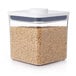 An OXO Good Grips clear square food storage container with brown rice inside.