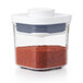 A clear OXO Good Grips square plastic food storage container with a white lid containing red powder.