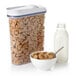 An OXO clear rectangular food storage container filled with cereal next to a bowl of cereal and a bottle of milk.