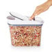 A hand using a white OXO food storage container to scoop cereal.