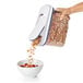 A hand pouring cereal from an OXO Good Grips container into a bowl.